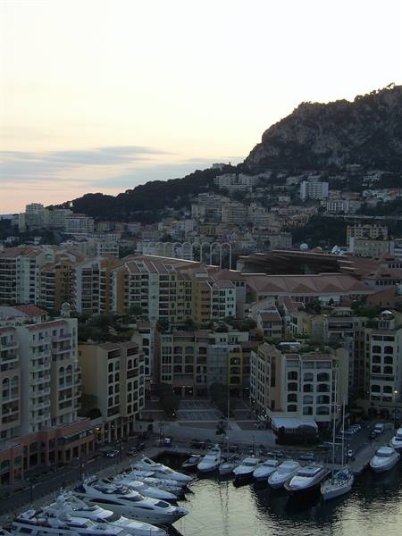 Yachts moored at Monaco harbor beneath buildings and rocky mountain