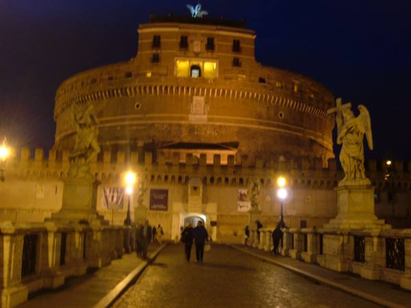 Castel Sant'Angelo illuminated at night, people walking on the angel bridge in Rome