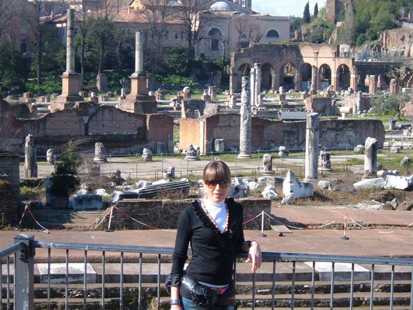 Woman by railing in front of Roman Forum ruins, columns and ancient marble in Rome
