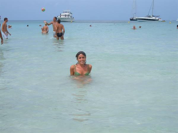 Woman in green bikini smiles in turquoise water, swimmers and boats nearby