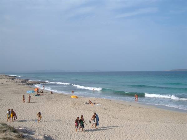 Beachgoers on light sand and turquoise water, some walking toward the waves