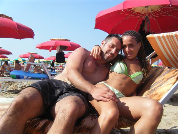 Couple in swimwear on sun lounger under red umbrellas on sunny beach
