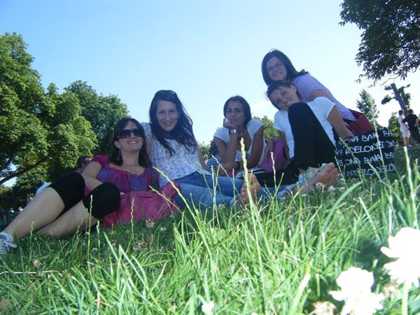 Five friends lying on grass in a sunny park, smiling against the light