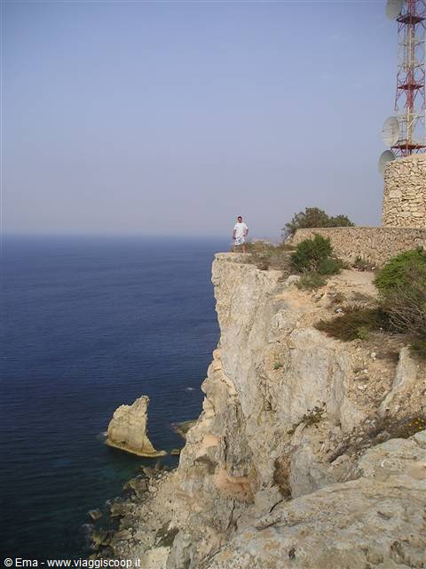 Tourist standing on the limestone cliff, blue sea and sea stack below