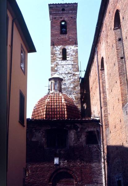 Stone and brick bell tower with terracotta dome among buildings in Lucca