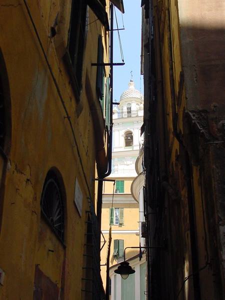 Narrow alley between ochre houses, church bell tower and dome, Genoa