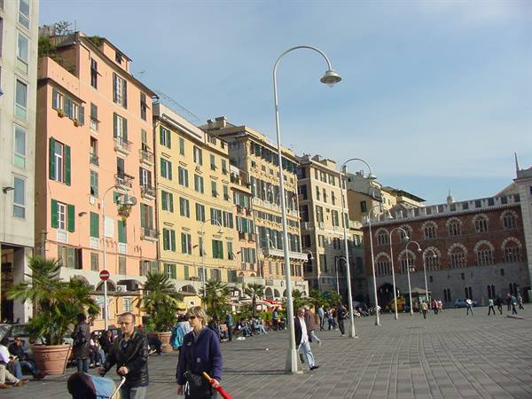 People strolling across Piazza de Ferrari in Genoa among colorful buildings and curved lampposts