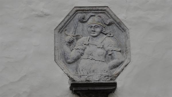 Octagonal stone relief of a warrior holding a sword, on a white wall