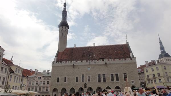 Tallinn's gothic Town Hall with tall tiled roof, market crowd under cloudy sky
