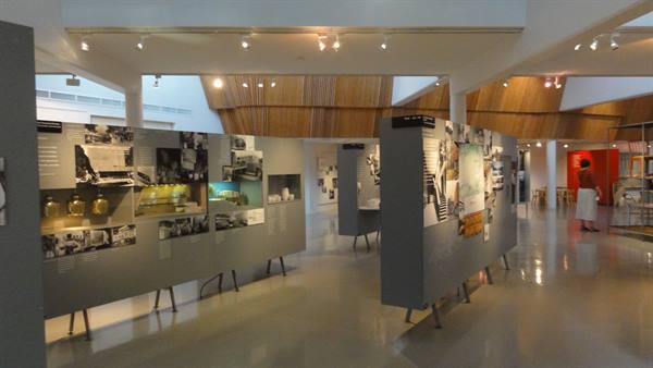 Grey display panels with photos and objects in a bright wooden museum