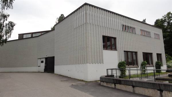 Modernist building clad in white tiles among trees, soft daylight