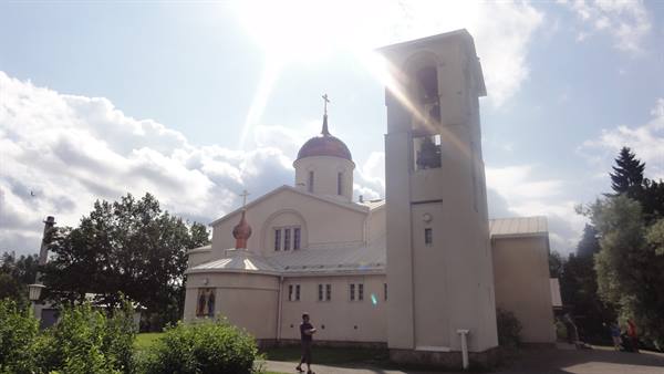 White Orthodox church with copper dome and bell tower, a man walks in the sunlight