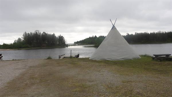 White cone tent on grassy lakeshore with wooden picnic table