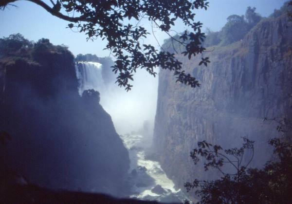 Victoria Falls, mist rising between rocky cliffs framed by leaves