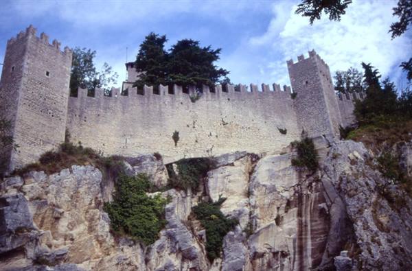 Crenellated walls of San Marino's Guaita tower on limestone cliff, cloudy sky