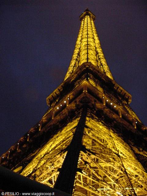 The Eiffel Tower glowing golden at night, seen from below against dark sky
