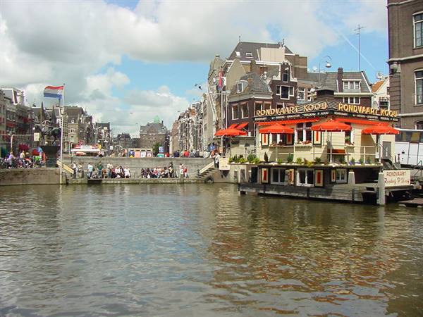 Amsterdam, floating café with red umbrellas on the canal, people on the quay