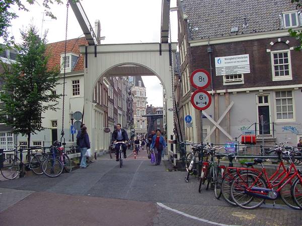 Wooden drawbridge in Amsterdam, parked bicycles and pedestrians passing under the white arch