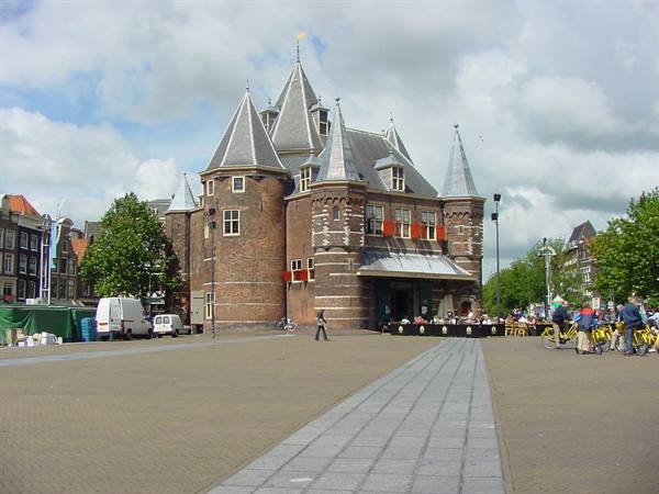 The brick Waag on Nieuwmarkt square, conical towers and bicycles under cloudy sky