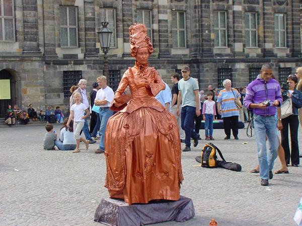 Copper-toned living statue performer on Dam square, Amsterdam, tourists passing by