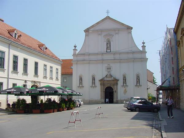 White baroque church facade, café umbrellas and parked cars in sunny square