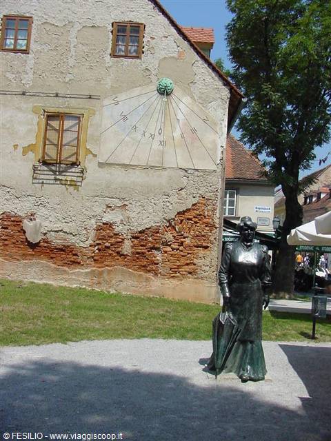 Bronze statue of a woman in front of old house with painted sundial