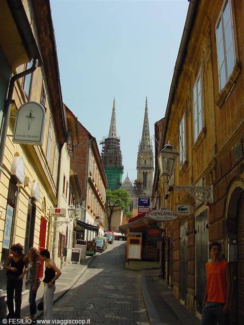 Cobbled street climbing toward Zagreb Cathedral among yellow buildings and kiosks