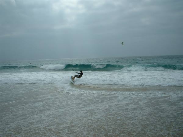 Kitesurfer riding turquoise waves, grey sky, foam on the shore
