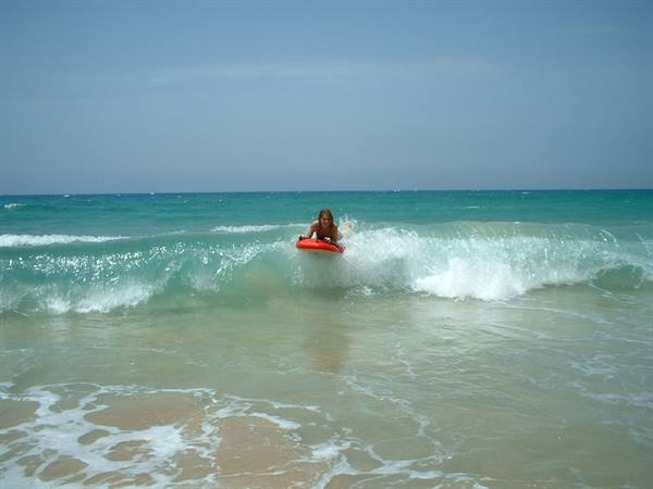 Woman on red bodyboard rides a turquoise wave near the shore