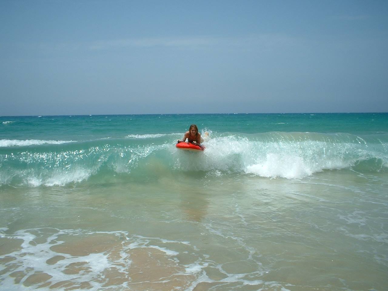 Woman on red bodyboard rides a turquoise wave near the shore