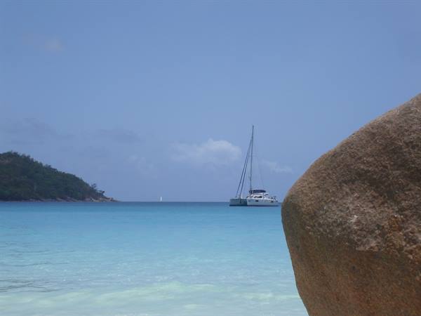 Catamaran anchored in turquoise water beside a large granite boulder, Seychelles
