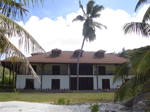 White colonial house with red roof among palms and sand