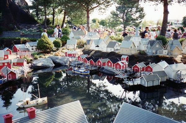 Miniature Lego village with red houses, boats and pond, visitors watching