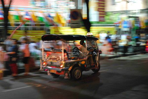 Tuk-tuk speeding at night past blurred Thai flags and lights