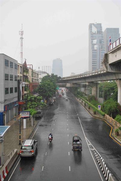 Rain-soaked street in Bangkok, tuk-tuk and motorbike under gray sky