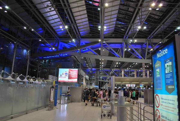 Travelers with carts in Suvarnabhumi airport hall, blue-lit steel roof