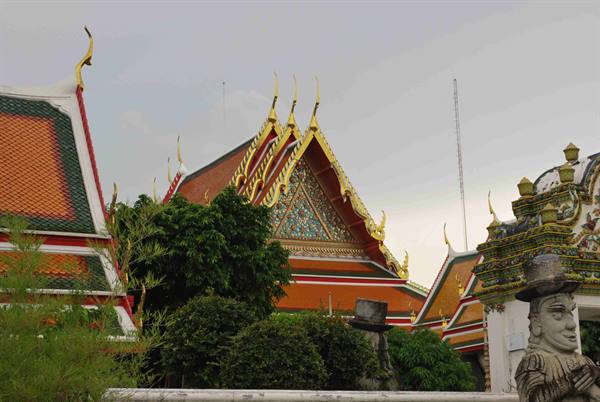 Golden roofs of Wat Pho temple among trees, stone guardian statue nearby