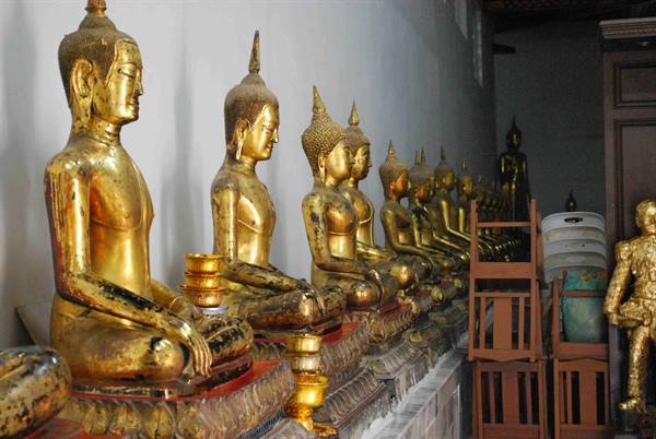 Row of seated golden Buddha statues, offering bowls beside, natural light