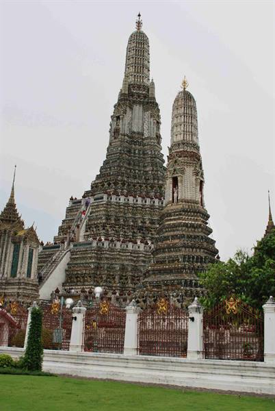 Wat Arun in Bangkok: porcelain-decorated prangs, grey sky, green lawn