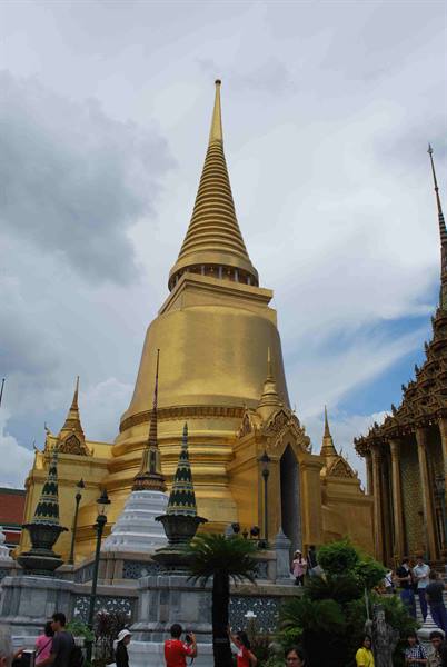 Tourists photograph the golden chedi of Wat Phra Kaew under cloudy skies