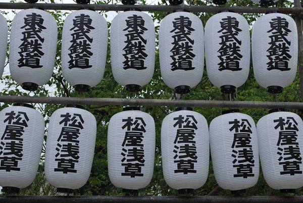 White paper lanterns with black Japanese characters hanging on metal frames