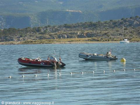 Two inflatable dinghies float on calm water before rocky hills