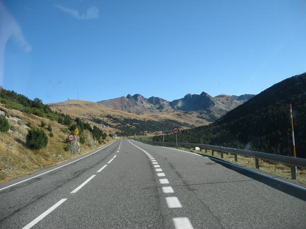 Asphalt road with guardrail toward rocky mountains and blue sky