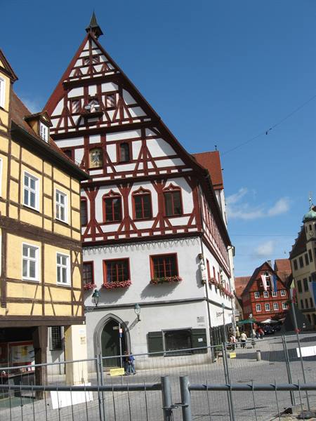 Red and white half-timbered house with flowers, sunny square, blue sky
