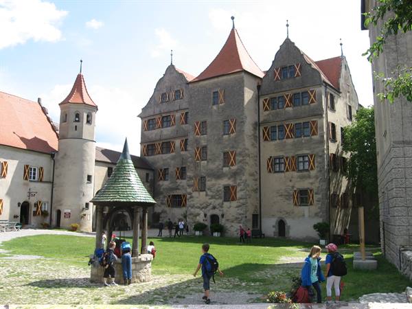 Children with backpacks in Harburg Castle courtyard, stone well, medieval facades