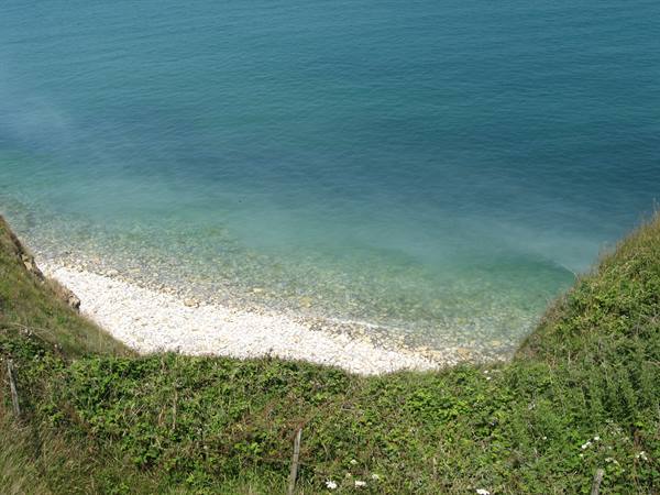 Small pebble cove with clear turquoise water and grassy slopes