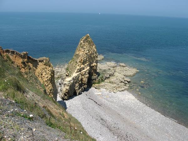 Rocky cliff over pebble beach, blue sea under clear sky
