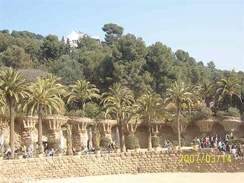 Palm trees and stone colonnade at Parc Güell, Barcelona, with visitors under sunny sky