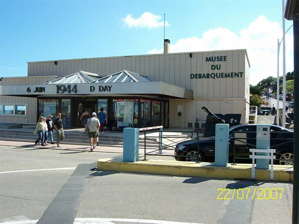 Tourists walk past the Musée du Débarquement under sunny skies