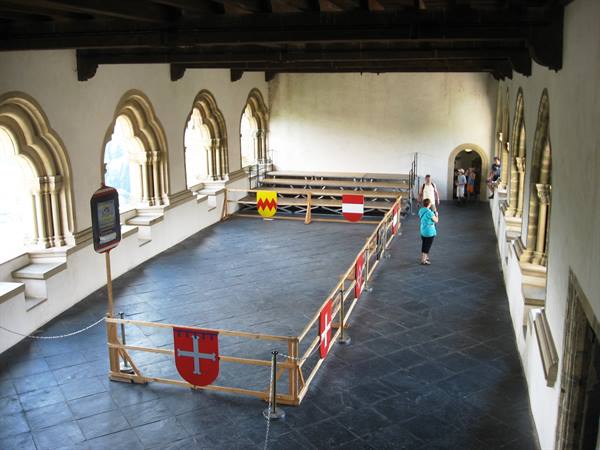 Tourist photographs a great hall with gothic arches and medieval banners
